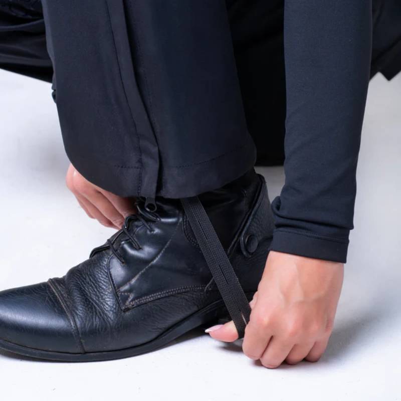 Person securing black dress shoe with Reinwear Reinpants Lite Black over black trousers.