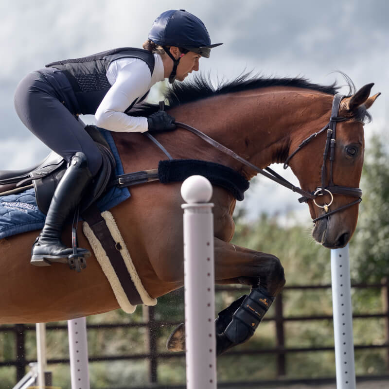 A rider in a Racesafe Motion Lite Adult Back Protector jumps a brown horse at an equestrian event.