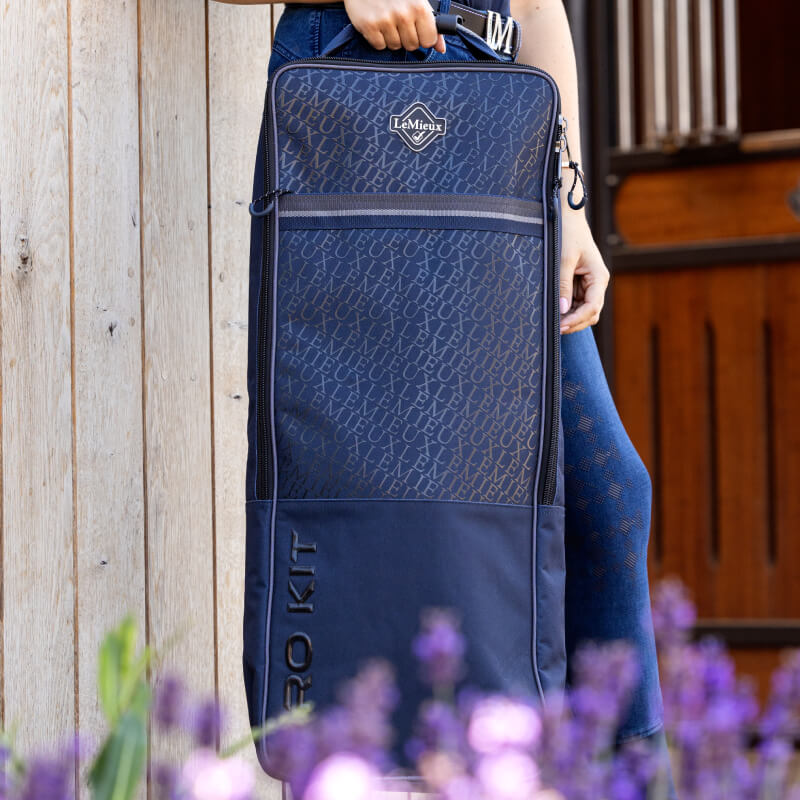 Someone holds a LeMieux Elite Pro Bridle Bag Navy outside a wooden stable.