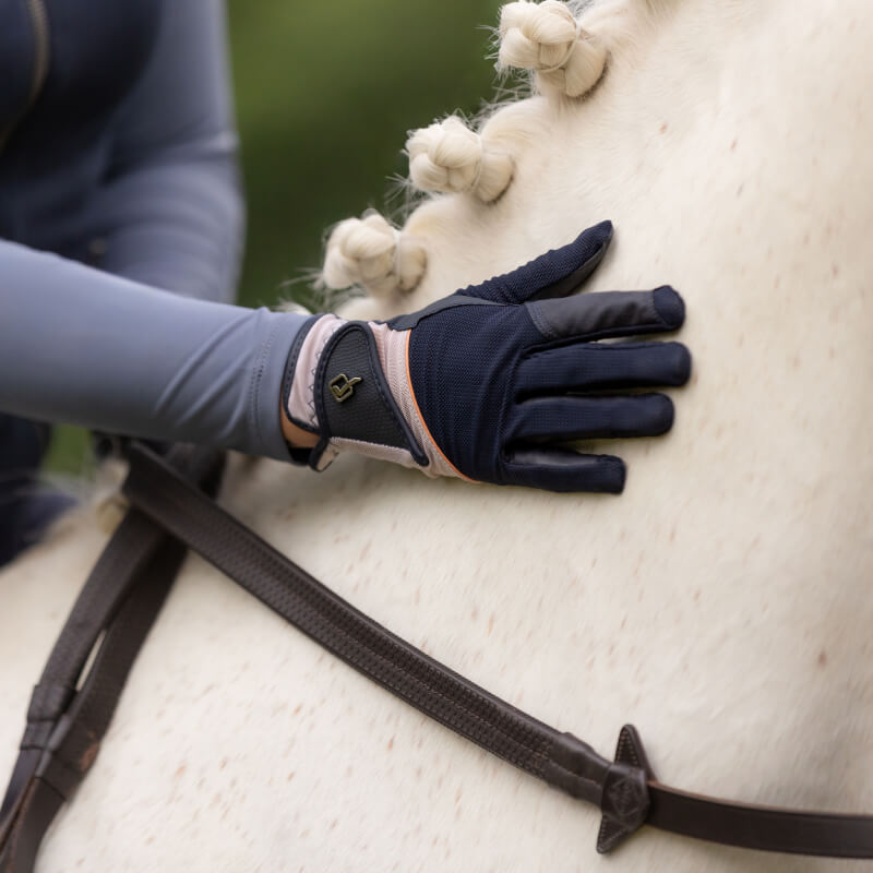 LeMieux Pro Mesh Glove Apricot/Navy grips a white horse’s braided mane on summer rides.