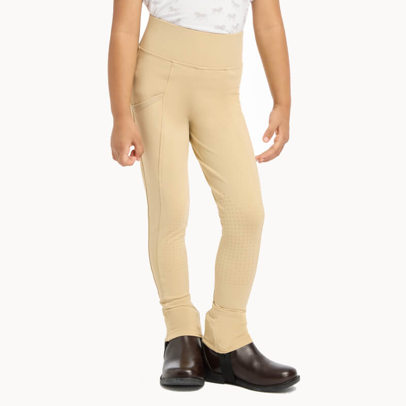 Child in LeMieux Mini Pull On Breech Beige, lightweight fabric, paired with brown boots.