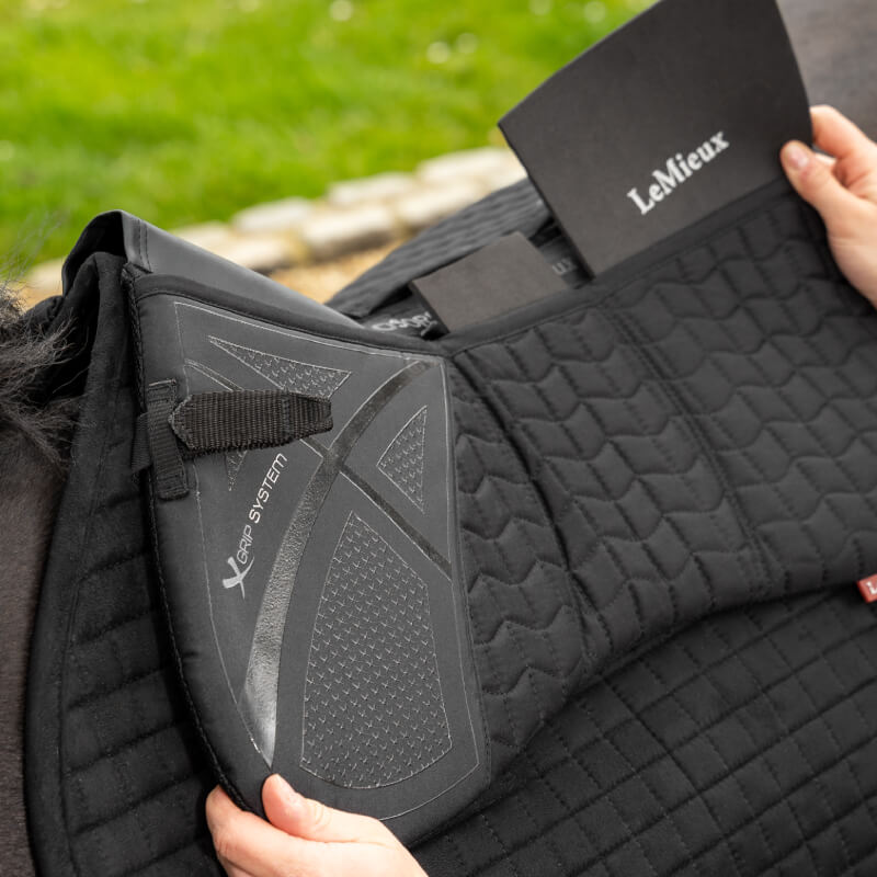 Someone inserts a LeMieux ProSorb Black Quilted Half Pad into a saddle pad.
