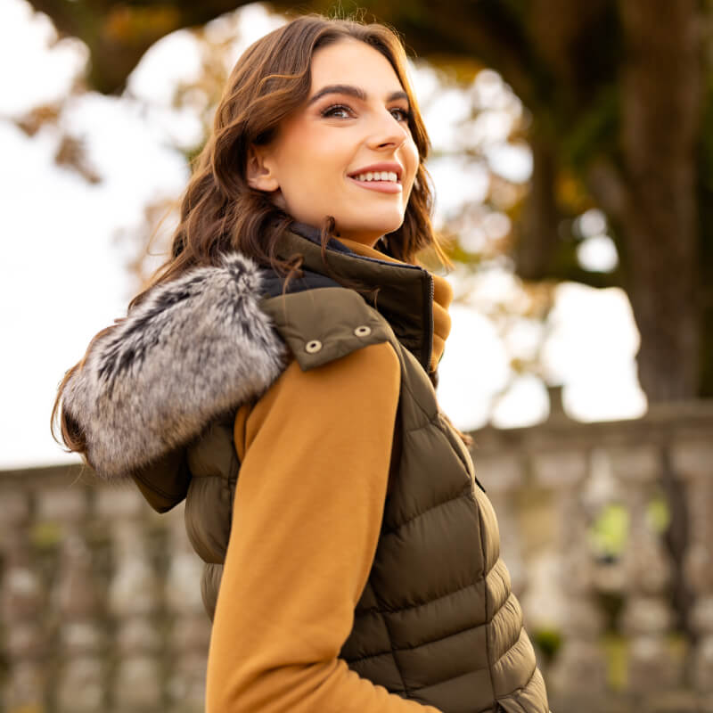 Woman in LeMieux Harper Longline Puffer Gilet Alpine walks through a park with autumn leaves.