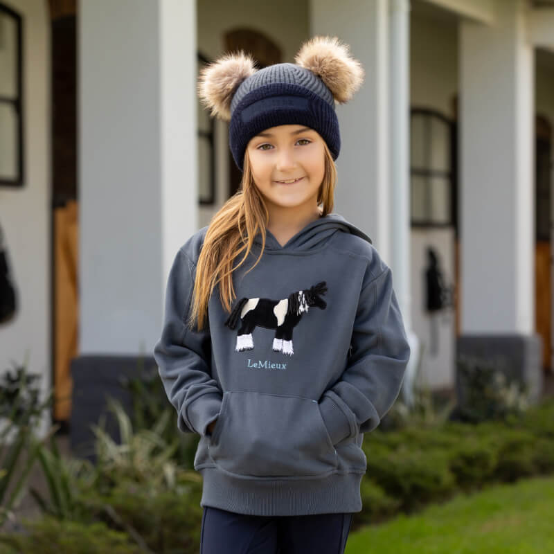 LeMieux Mini Clara Beanie Petrol: Petrol kids beanie with black cuff and tan faux fur pom-poms.