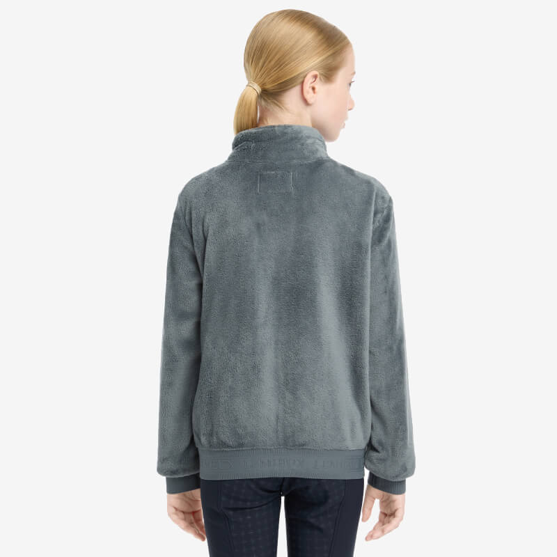 Girl with blonde ponytail in LeMieux Young Rider Libby Fleece Petrol, seen from the back.