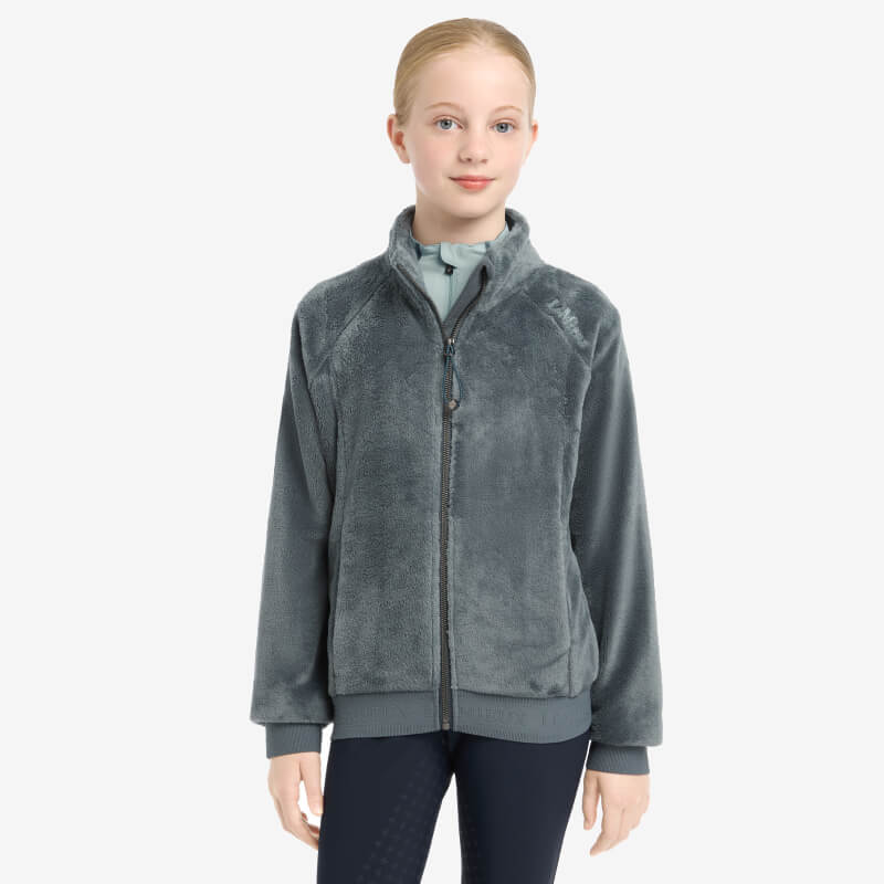 Young rider in a LeMieux Libby Fleece Petrol jacket and black pants against a white background.