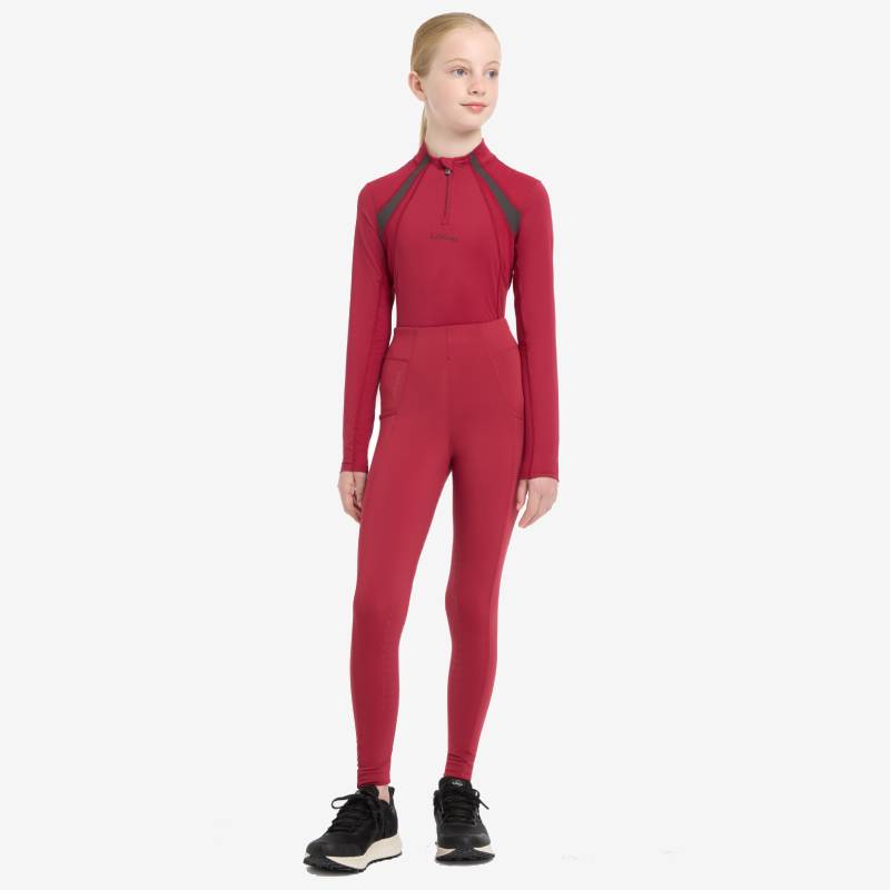 Young rider wears LeMieux Young Rider Mia Mesh Baselayer Ember, with black sneakers.