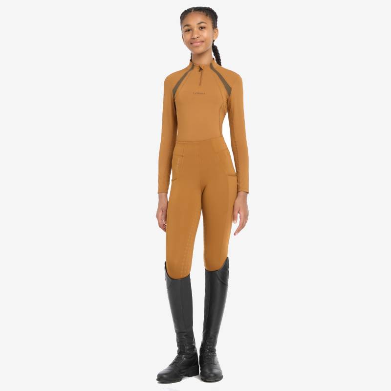 A young woman smiles in a LeMieux Young Rider Mia Mesh Baselayer Ginger, ready to ride.