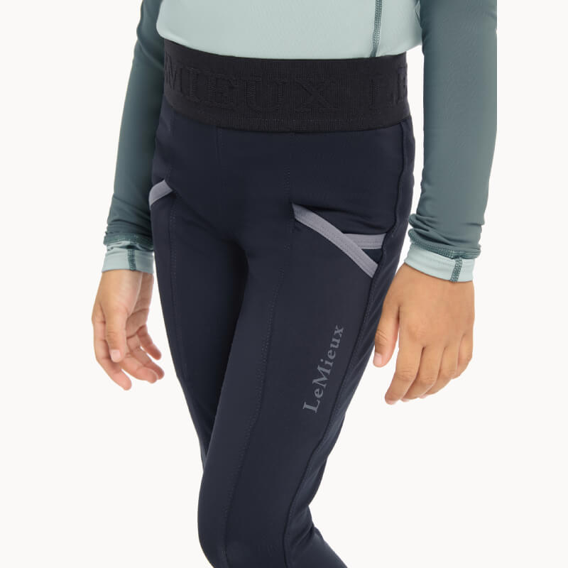 Child in LeMieux Mini Pull Ons Navy breeches and grey top, shown shoulders to knees.