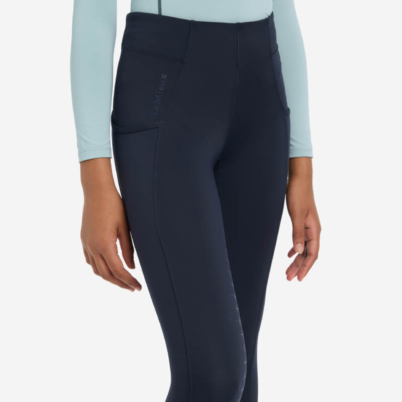 Person in LeMieux Young Rider Orla Pull Ons Navy leggings, black sneakers, and a light blue top.