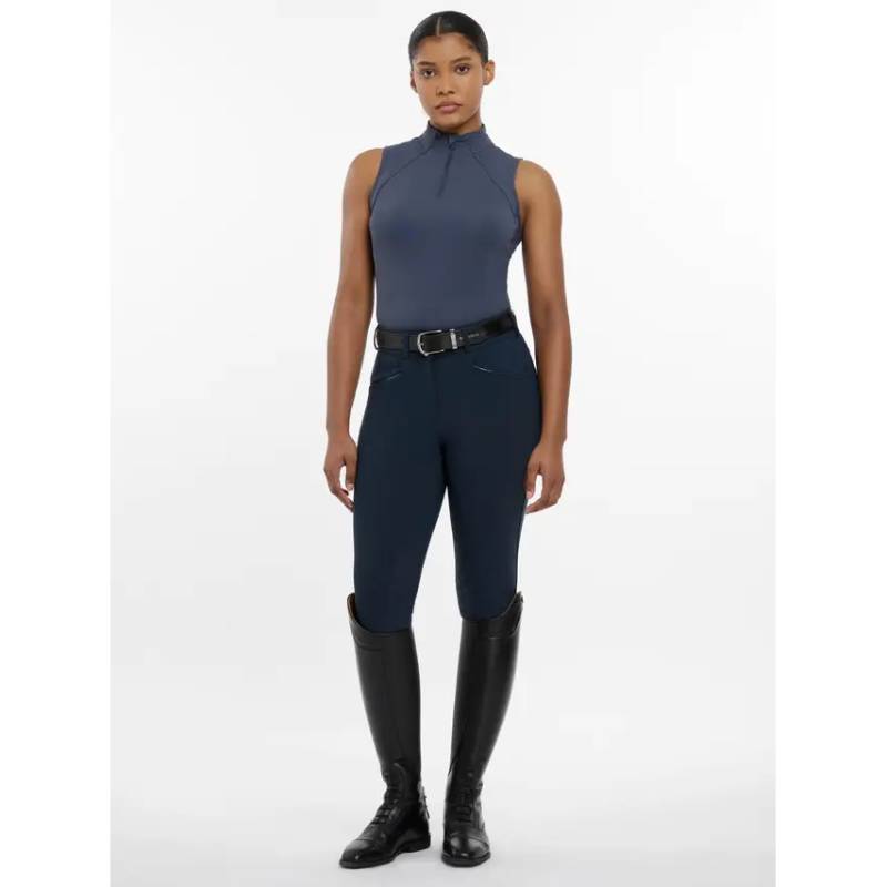 A woman in LeMieux Maria Mesh Sleeveless Baselayer Dusk Blue and tall black boots.