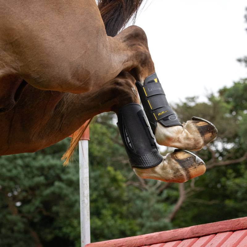 A horse in LeMieux MIMSafe Boot Hind Black jumps a red fence, showing equestrian sport.
