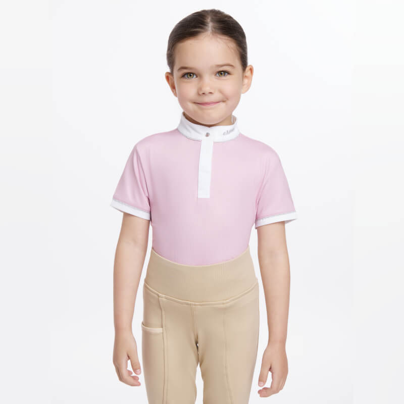 Child in LeMieux Mini Bella Show Shirt Blossom and beige pants smiles against plain background.