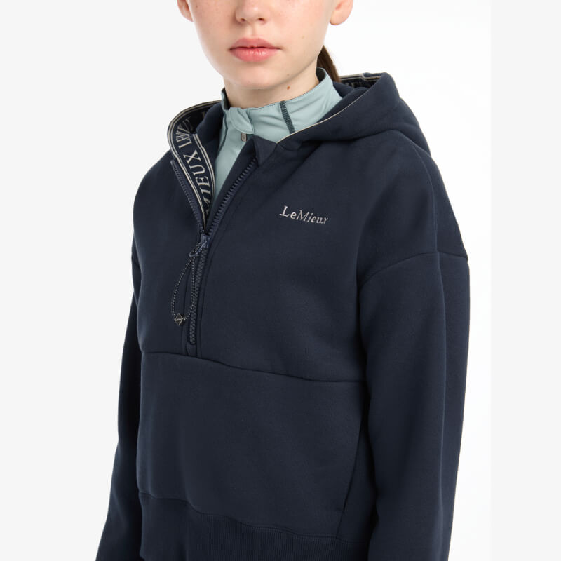 Girl in a navy LeMieux Young Rider Hettie Half Zip Hoodie over a light blue collared shirt.