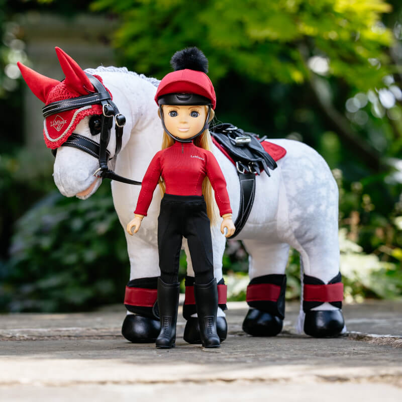 LeMieux Toy Rider Chloe stands in riding gear by a toy horse with red and black tack.