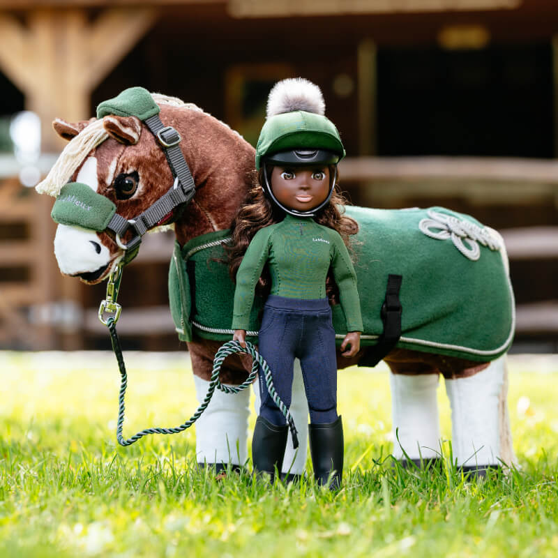 LeMieux Toy Rider Maya stands by a horse toy, both in green outfits, on grass.