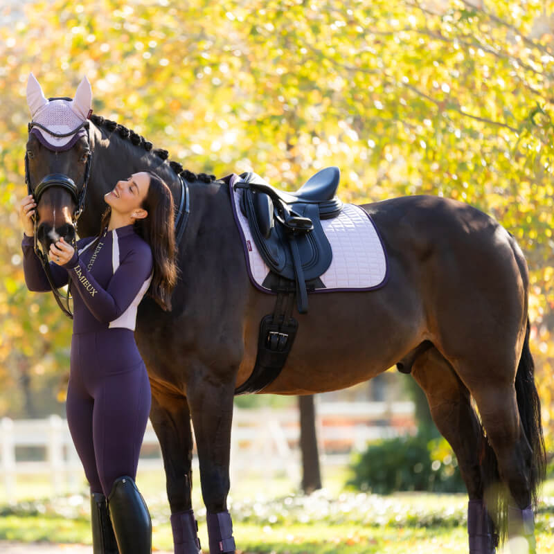 Woman in riding gear hugs her horse with a LeMieux Suede Dressage Square Lilac saddle pad.