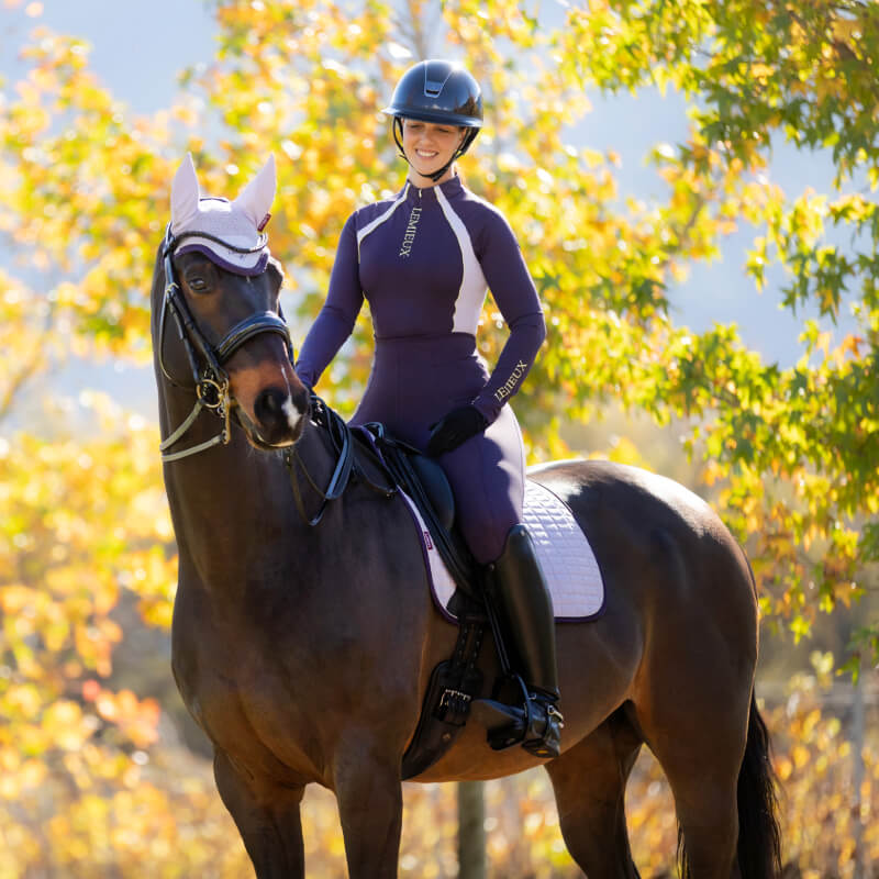 Smiling rider in lilac LeMieux Suede Dressage Square on a dark brown horse outdoors.