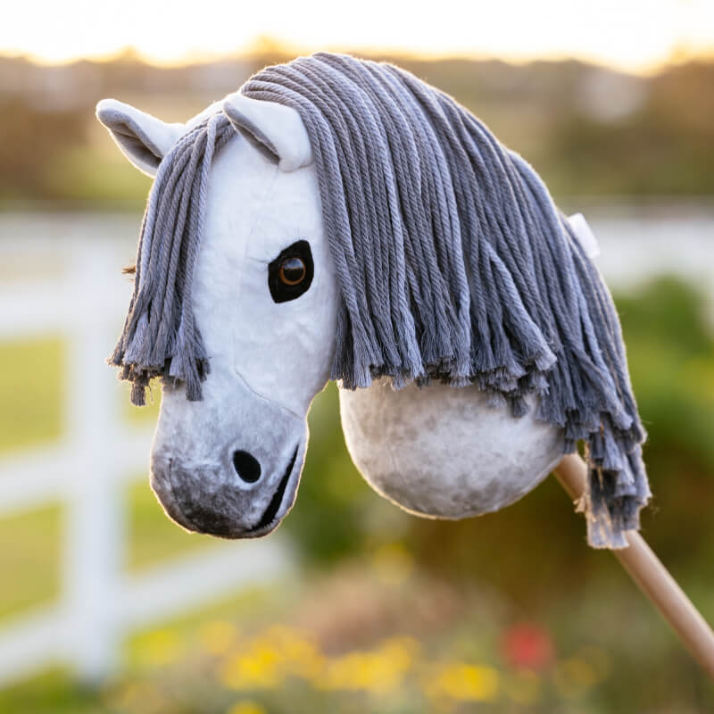 LeMieux Hobby Horse Earl with gray yarn mane stands outdoors near a white fence.