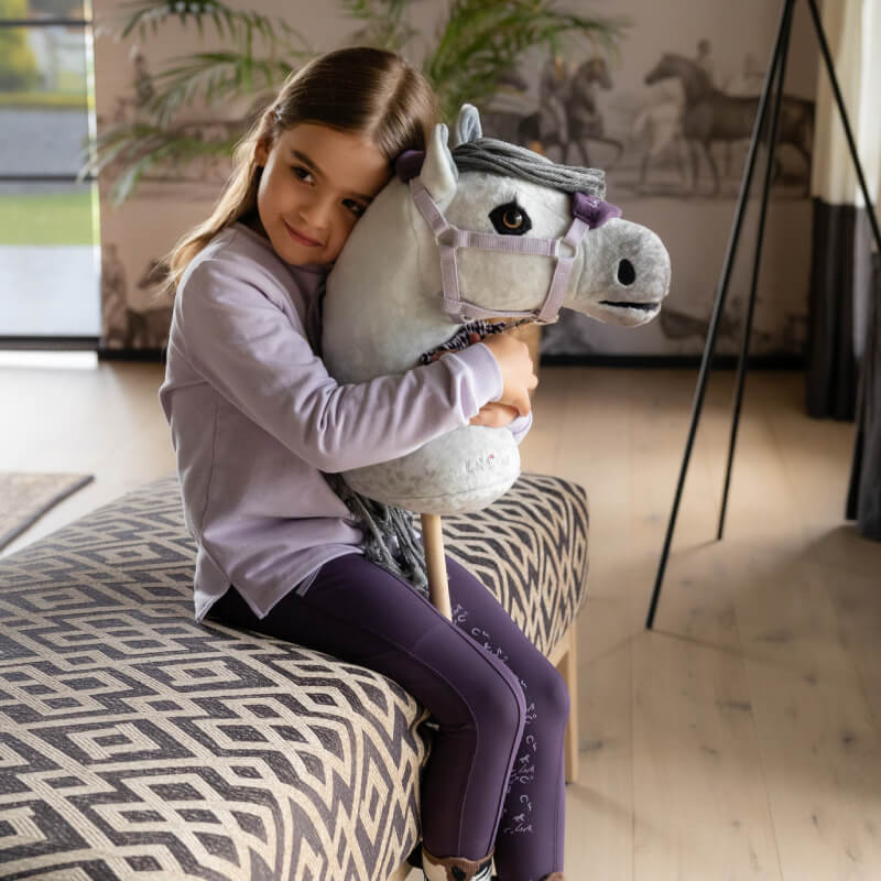 Young girl hugs LeMieux Hobby Horse Earl, a hand-finished riding toy, indoors.