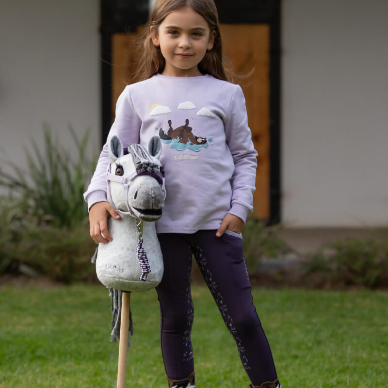 Smiling girl on grass holds a hand-finished LeMieux Hobby Horse Earl by LeMieux.