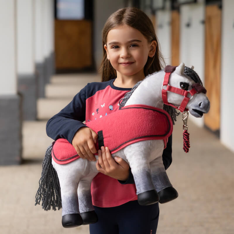 Smiling girl holds a LeMieux Toy Pony Blanca with red bridle and blanket.
