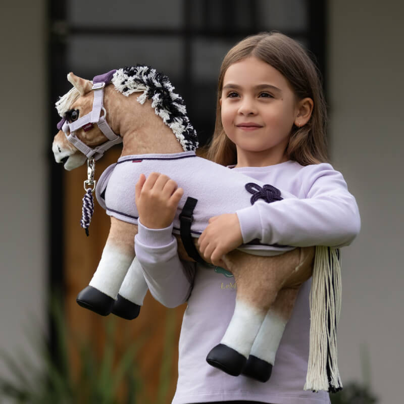 Smiling girl holding a LeMieux Toy Pony Oskar by LeMieux while standing outside.