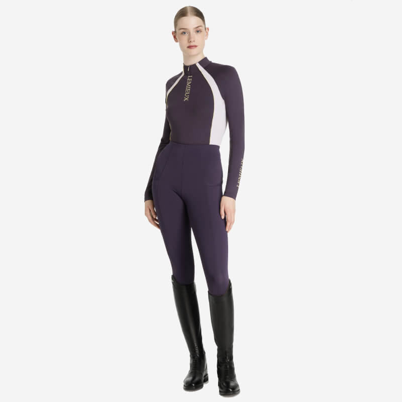 Woman in a LeMieux Phillipa Mesh Baselayer Juniper with tall black riding boots.