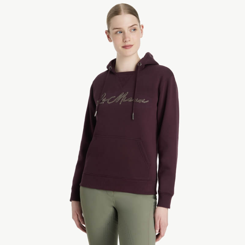 Woman in a LeMieux Elspeth Hoodie Damson enjoys autumn trees outdoors.