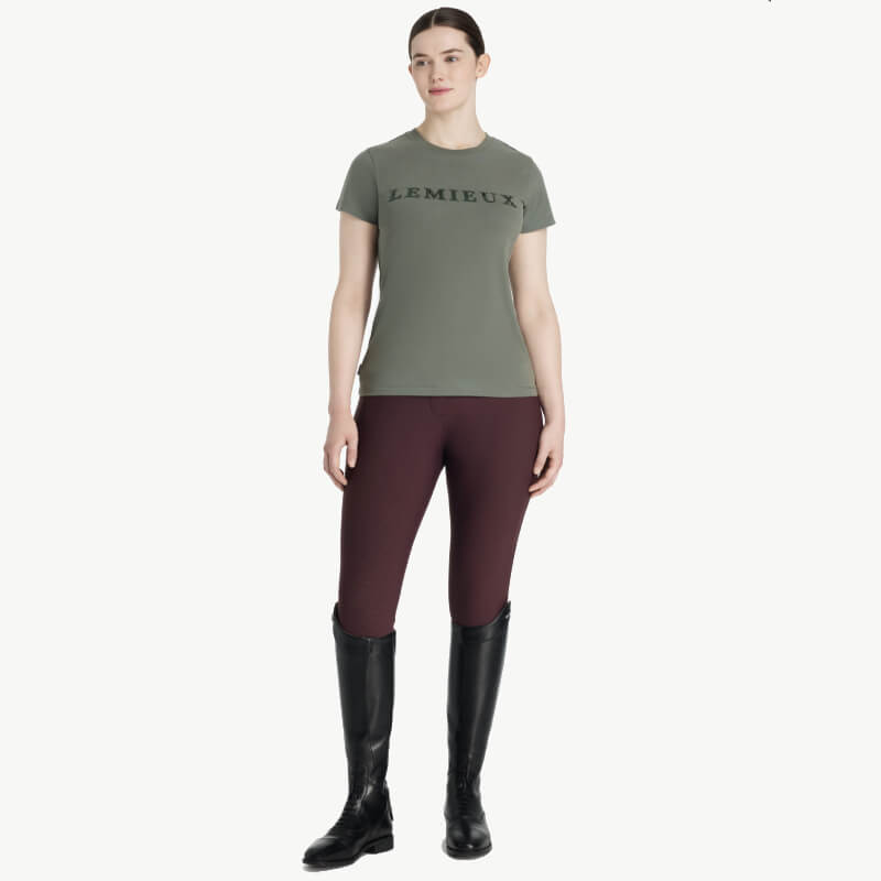 Woman stands forward in LeMieux Classique Sparkle T-Shirt Rosemary, burgundy pants, black boots.