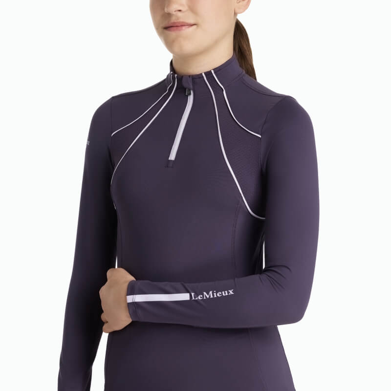 Girl in LeMieux Young Rider Mia Mesh Baselayer Juniper with white piping and branding on sleeve.