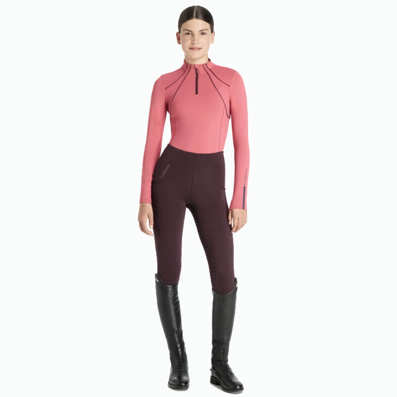 Girl wearing LeMieux Young Rider Mia Mesh Baselayer Cranberry, facing forward in dark leggings.