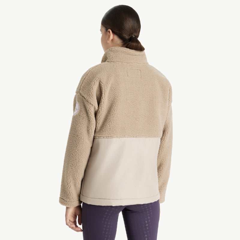 Woman in a LeMieux Tammy Teddy Fleece Almond and tan jacket, dark hair tied back, facing away.