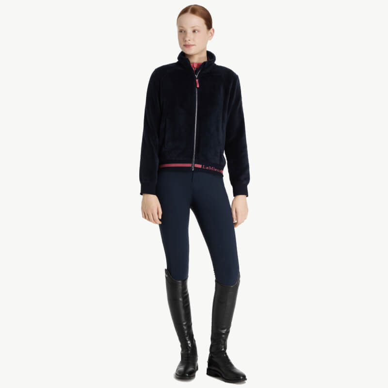 Woman in LeMieux Young Rider Libby Fleece Navy, navy pants, and black knee-high boots standing.