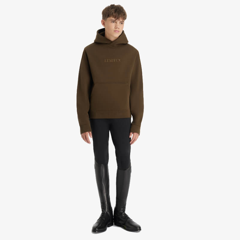 Young rider in a LeMieux Young Rider Boys Hoodie Alpine, black pants, and tall black boots.