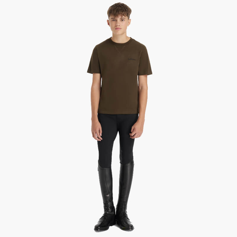 Teen boy in a LeMieux Young Rider Boys T-Shirt Alpine, black pants, and tall boots on white.