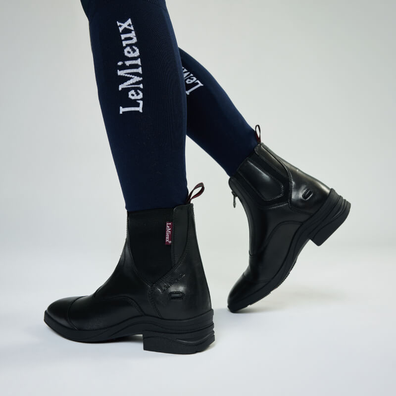 LeMieux Junior Zip Paddock Boot Black with navy LeMieux socks, shown on a child’s lower legs.