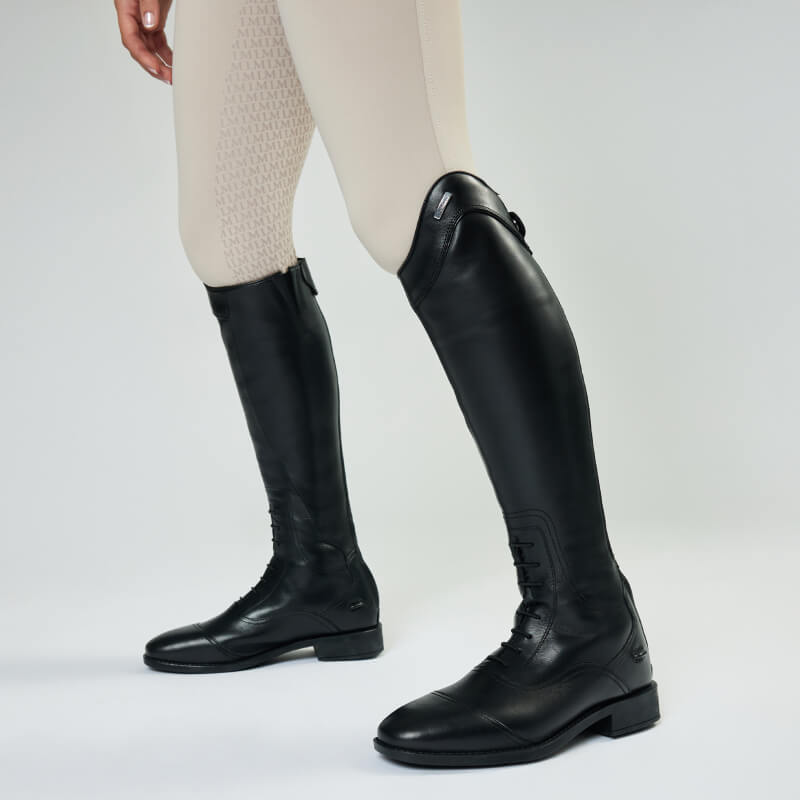 Person wearing beige riding pants and LeMieux Junior Field Riding Boot Black against a plain background.