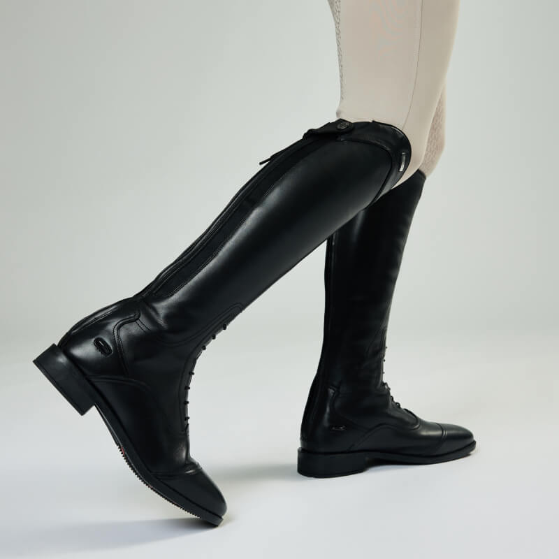 Person wearing beige pants and LeMieux Junior Field Riding Boot Black on a white background.