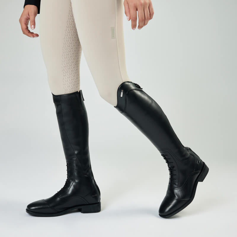 Person wearing LeMieux Junior Field Riding Boot Black with beige riding pants on a light background.