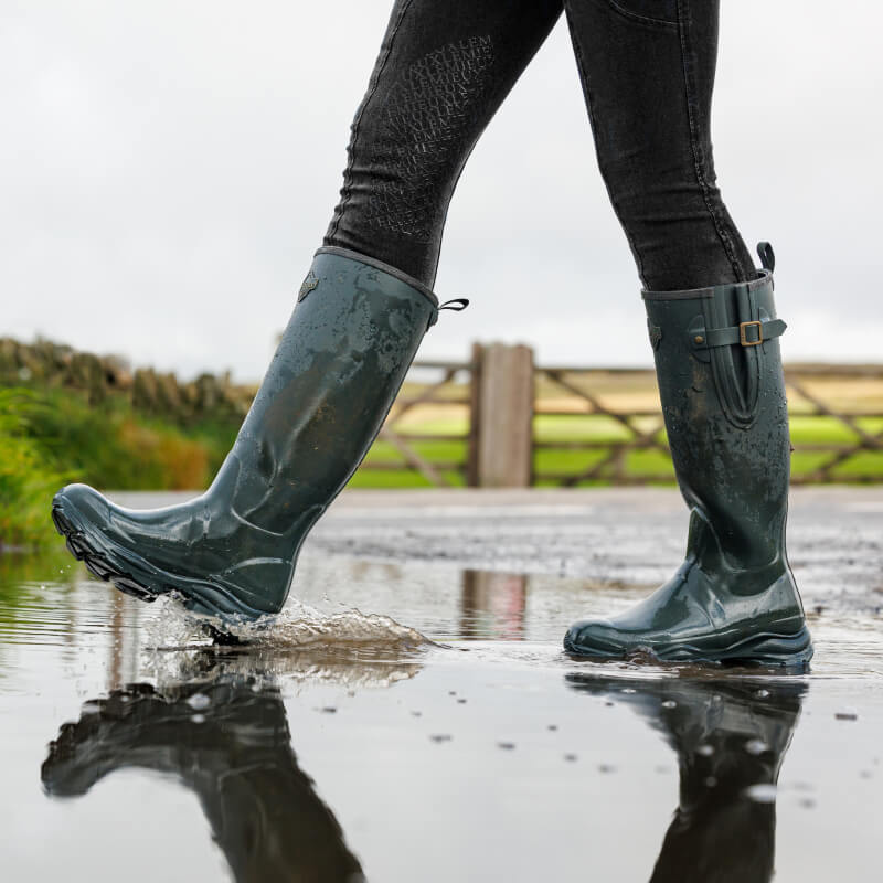 Person walking in LeMieux Ultra Stride Wellington Boots Oak through a wet outdoor path.