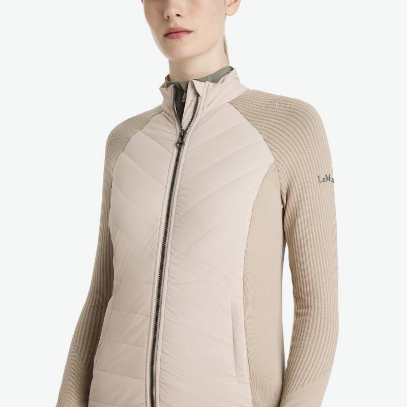 Woman wears the LeMieux Maddie Jacket Stone with ribbed sleeves and logo on the arm.