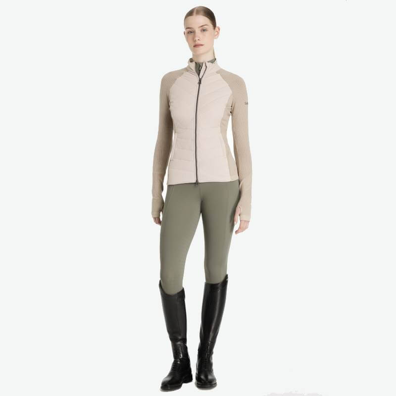 Woman in a LeMieux Maddie Jacket Stone, olive riding pants, and black knee-high boots.