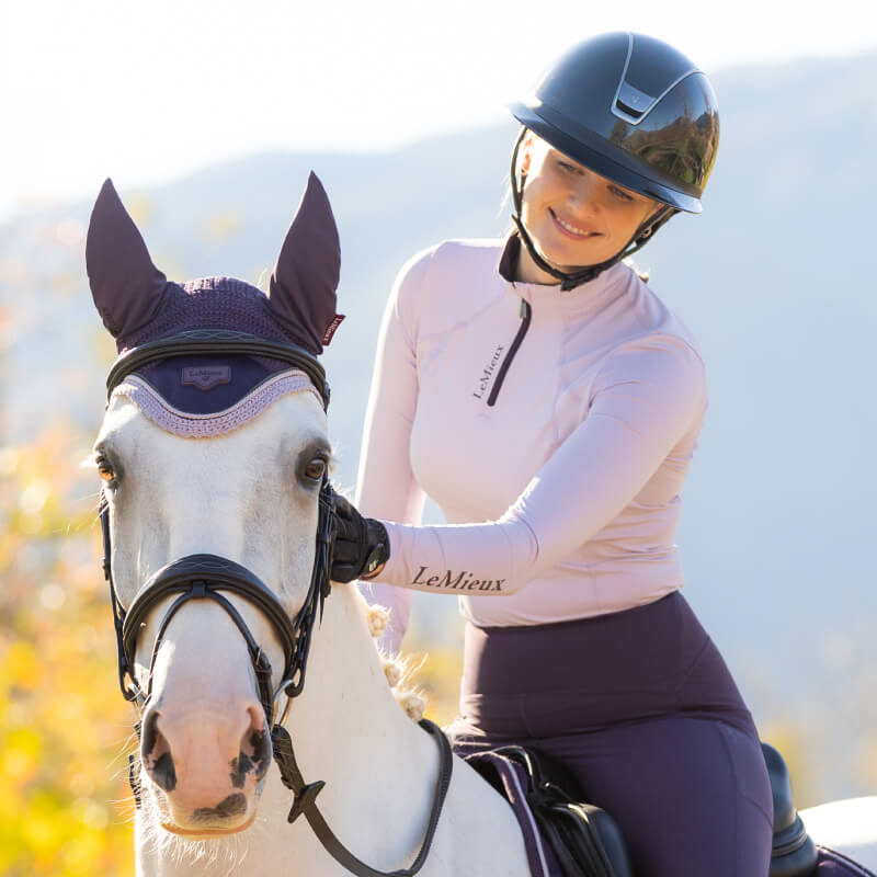 Woman smiles in a LeMieux Classique Baselayer Lilac, paired with dark pants.