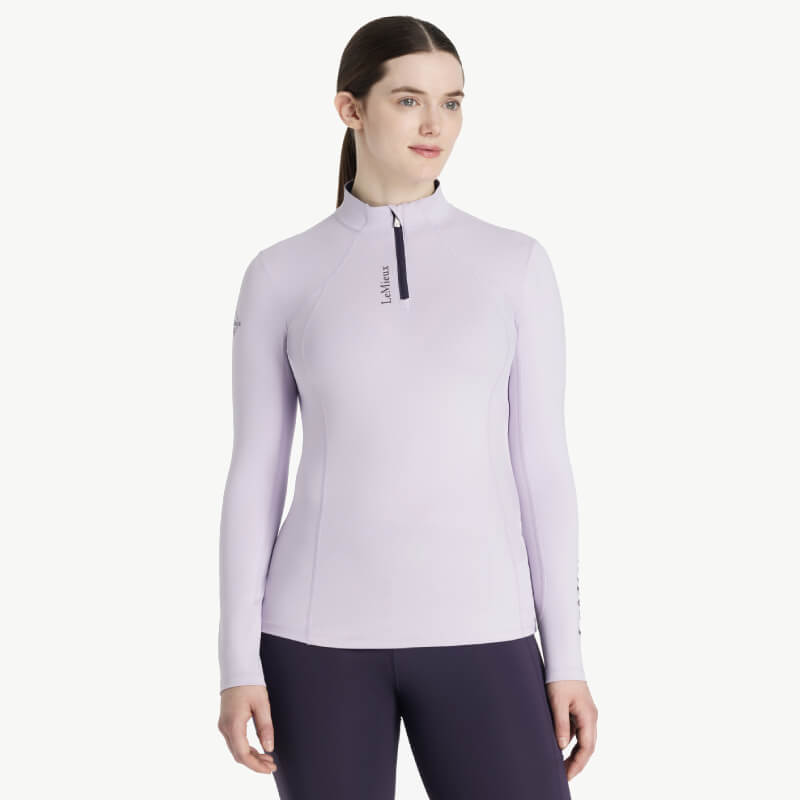 Woman smiles in a LeMieux Classique Baselayer Lilac, paired with dark pants.