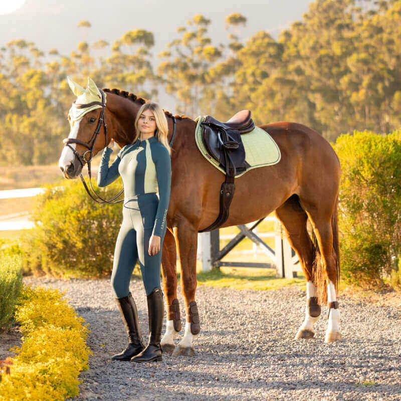 Woman in riding gear stands by a saddled horse with a LeMieux Suede Close Contact Square Macaron.