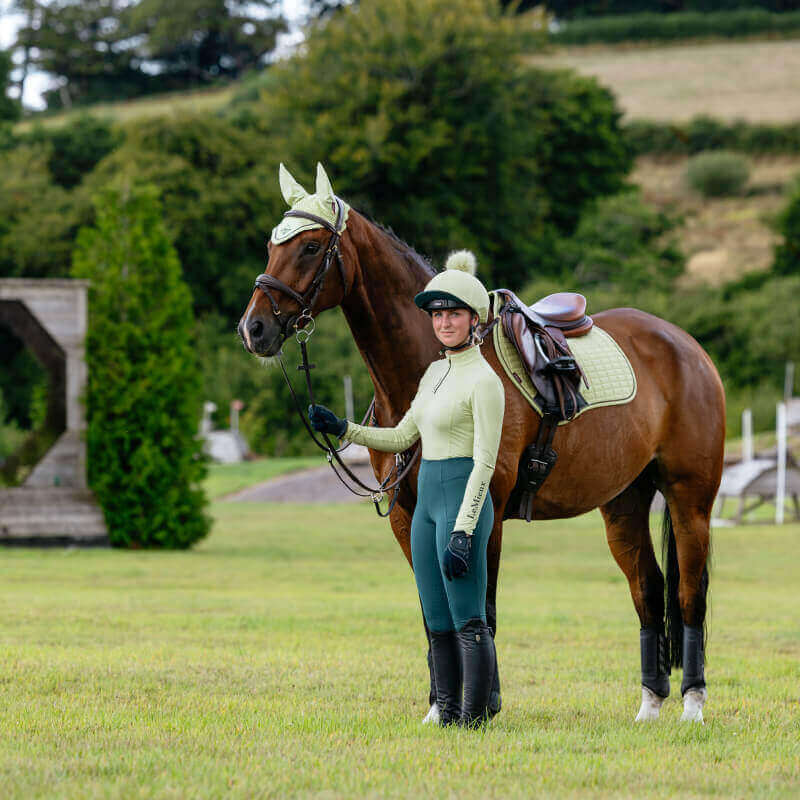 Woman in riding gear beside a brown horse wears LeMieux Suede Close Contact Square Macaron.