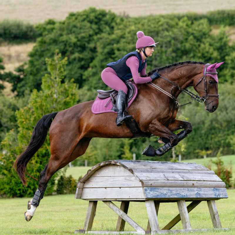 Rider in purple jumps with horse using the LeMieux Suede Close Contact Square Mallow pad.