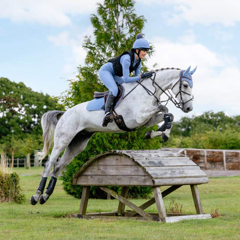 Rider jumping gray horse outdoors with LeMieux Suede Close Contact Square in Powder Blue.