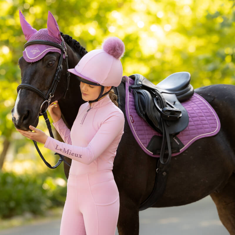 Girl in pink riding gear with a black horse and LeMieux Suede General Purpose Square Mallow.